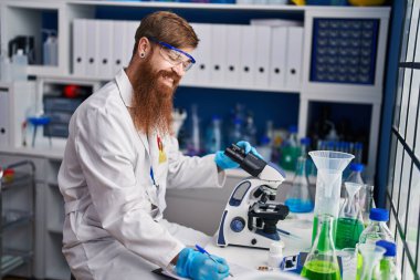 Genç kızıl saçlı bilim adamı laboratuarda çalışan mikroskop yazısı kullanıyor.