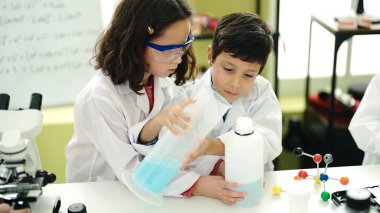 Sevimli bir oğlan ve kız öğrenci laboratuvar sınıfında test tüpüne sıvı döküyorlar.