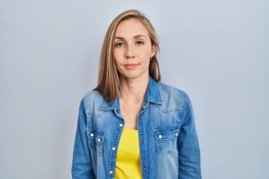 Mavi arka planda duran genç sarışın kadın yüzünde ciddi bir ifadeyle rahatlamış. Basit ve doğal bir şekilde kameraya bakıyorsun.. 