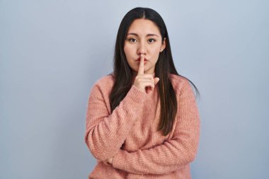 Young latin woman standing over blue background asking to be quiet with finger on lips. silence and secret concept. 