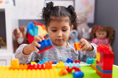 Anaokulundaki masada oturan, inşaat bloklarıyla oynayan sevimli İspanyol kız.