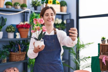 Genç bayan çiçekçi çiçekçi dükkanında akıllı telefon fabrikasıyla selfie çekiyor.