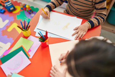 Sevimli erkek ve kız anaokulu öğrencileri anaokulunda masa başında oturmuş defter çiziyorlar.