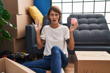 Esmer bir kadın elinde yeni evin ve domuz kumbarasının anahtarlarını tutuyor. Şok olmuş bir halde. Şüpheci ve alaycı görünüyor. 