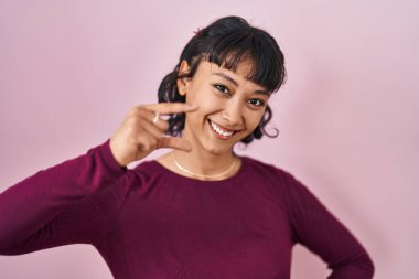Pembe arka planda duran genç ve güzel bir kadın gülümsüyor ve kendinden emin bir şekilde el hareketleriyle küçük boy işareti yapıyor ve kameraya bakıyor. ölçüm kavramı. 