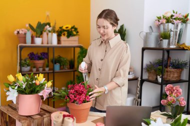 Genç beyaz kadın çiçekçi çiçekçide dağıtıcı sulama bitkisi kullanıyor.