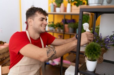 Young hispanic man florist smiling confident holding plants at flower shop