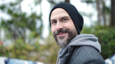 Genç kel adam parkta kendine güvenerek gülümsüyor.