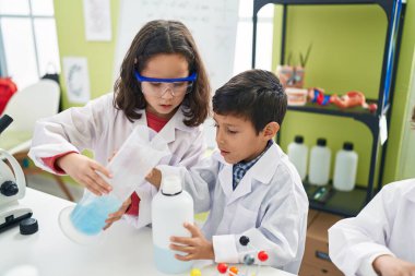 Sevimli bir oğlan ve kız öğrenci laboratuvar sınıfında test tüpüne sıvı döküyorlar.
