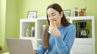 Genç beyaz kadın yemek odasında laptopunu kullanıyor.