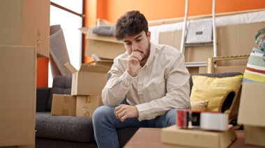 Yeni evinde ciddi bir ifadeyle koltukta oturan İspanyol asıllı genç adam.