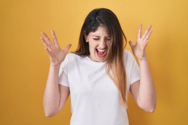 Sarı arka planda duran genç esmer kadın başarı için çıldırıyor ve çıldırıyor kollarını kaldırıyor ve gözleri kapalı heyecanla bağırıyor. Kazanan konsept 