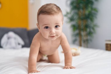Yatak odasında beyaz bebek yatakta emekliyor.