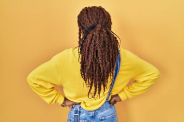Sarı arka planda dikilen Afrikalı kadın geriye doğru bakıyor kolları vücudunda. 