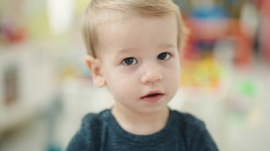 Adorable blond toddler standing with relaxed expression at kindergarten