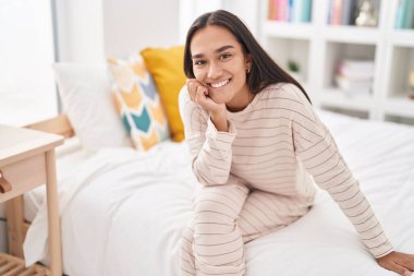 Genç, güzel, İspanyol bir kadın yatakta kendinden emin bir şekilde oturuyor.