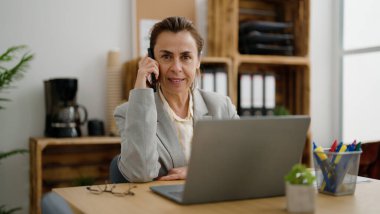 Orta yaşlı İspanyol iş kadını ofisteki akıllı telefondan konuşuyor.