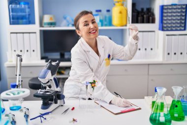 Laboratuardaki panoda bitki yazısıyla test tüpü tutan orta yaşlı bir bilim kadını.