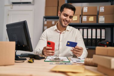 Genç İspanyol iş adamı. Ofiste akıllı telefon ve kredi kartı kullanıyor.