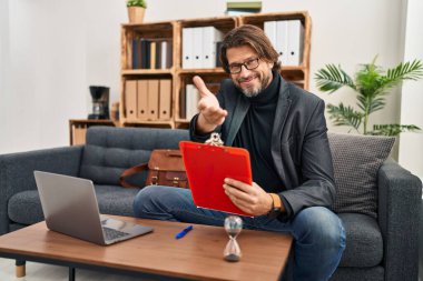 Muayenehanede çalışan yakışıklı, orta yaşlı bir adam neşeli bir gülümsemeyle avuç içi yardım ve kabullenme sunuyor.. 