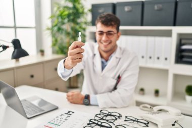 Young hispanic man optician smiling confident holding eye drops at clinic