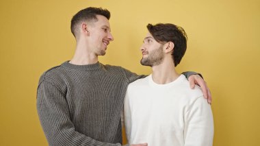 Birbirlerine sarılan iki erkek izole edilmiş sarı arka planda duruyor.