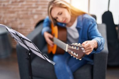Genç sarışın müzisyen müzik stüdyosunda klasik gitar çalıyor.