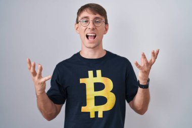 Bitcoin tişört giyen beyaz, sarışın bir adam başarının çılgınlığını kollarını kaldırarak ve gözleri kapalı heyecanla bağırarak kutluyor. Kazanan konsept 