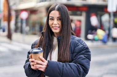 Young beautiful hispanic woman smiling confident drinking coffee at street
