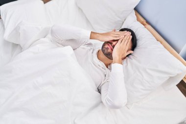 Young hispanic man stressed lying on bed at bedroom
