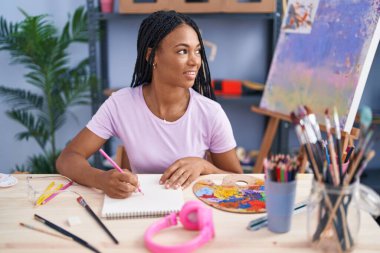 Sanat stüdyosunda kendine güvenen, gülümseyen Afrikalı Amerikalı kadın sanatçı.