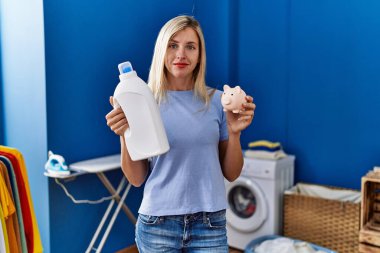 Çamaşır deterjanı şişesi tutan güzel bir kadın ve yüzünde ciddi bir ifadeyle rahatlamış bir domuz kumbarası. Basit ve doğal bir şekilde kameraya bakıyorsun.. 