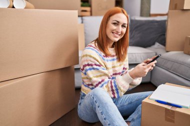 Young caucasian woman using smartphone sitting on floor at new home