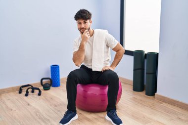 Sakallı İspanyol bir adam yoga odasında pilatese oturmuş kameraya kendinden emin kollarını kavuşturmuş ve çenesini kaldırmış gülümsüyor. Olumlu düşünmek. 
