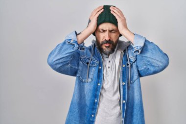 Ağrı ve migren yüzünden başı ağrıyan, başı ağrıyan, yün şapka takan İspanyol dövmeli genç bir adam. Eller başının üstünde.. 