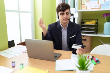 Non binary man call center agent using computer and credit card working at office