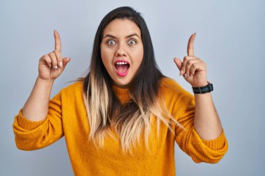 Soyutlanmış arka planda duran genç İspanyol kadın şaşırmış, şaşırmış ve parmaklarıyla işaret ediyor ve kollarını kaldırıyordu.. 