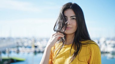 Genç, güzel, İspanyol bir kadın, deniz kenarında sakin bir ifadeyle duruyor.