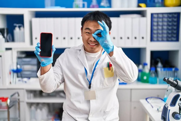在科学家实验室工作的中国年轻人 拿着智能手机 高兴地微笑着 手拿着手机 手拿着标牌 用手指看 — 图库照片