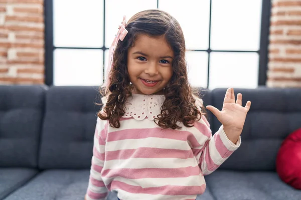 Adorable Hispanic Girl Saying Hello Hand Sitting Sofa Home — Stockfoto