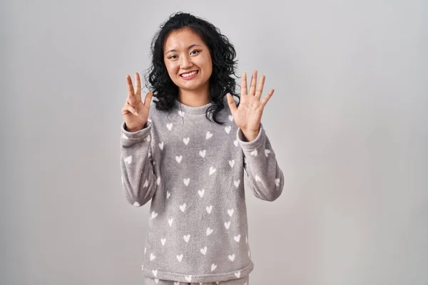 自信満々で笑顔ながらパジャマ姿の若いアジア人女性が指ナンバー8で指差す — ストック写真
