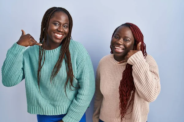 青い背景の上に立っている2人のアフリカ人女性は 電話で話すような手と指で電話のジェスチャーをして笑っています コミュニケーションの概念 — ストック写真