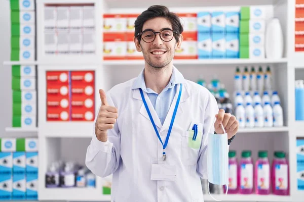 Young Hispanic Man Working Pharmacy Drugstore Holding Safety Mask Smiling — Stock Photo, Image