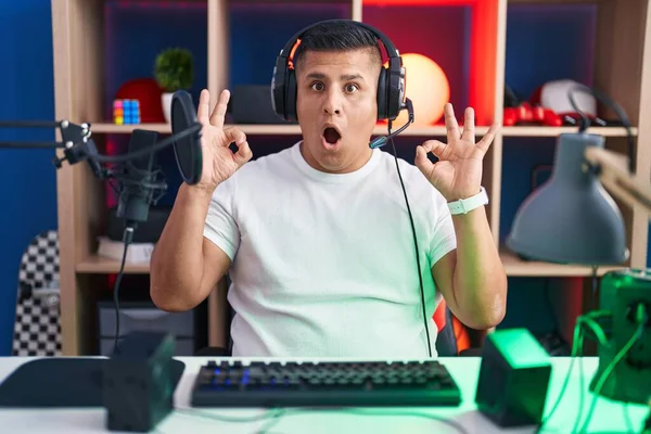 Молодой Латиноамериканец Играющий Видеоигры Выглядит Удивленным Шокированным Делая Хорошо Символ — стоковое фото