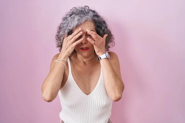 中年妇女灰白的头发站在粉红的背景上揉揉眼睛以消除疲劳和头痛 困倦和疲倦的表情 视力问题 — 图库照片