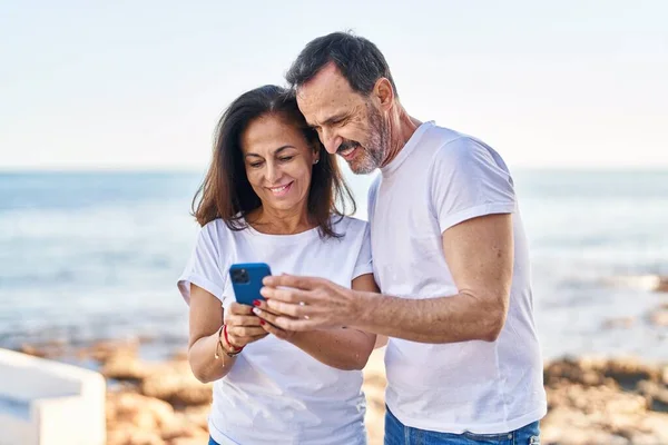 中世の男性と女性のカップルが一緒に海辺に立ってスマートフォンを使用して — ストック写真