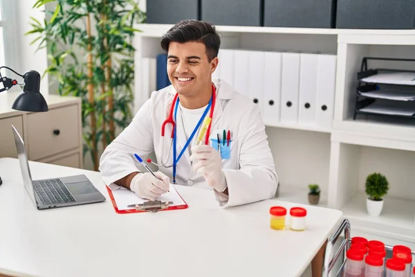 Young Hispanic Man Doctor Writing Medical Report Holding Urine Test — Zdjęcie stockowe