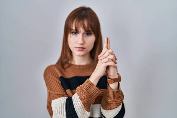 Young beautiful woman wearing striped sweater over isolated background holding symbolic gun with hand gesture, playing killing shooting weapons, angry face