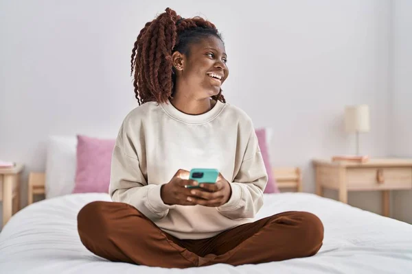 Afroamerykanka Pomocą Smartfona Siedzi Łóżku Sypialni — Zdjęcie stockowe