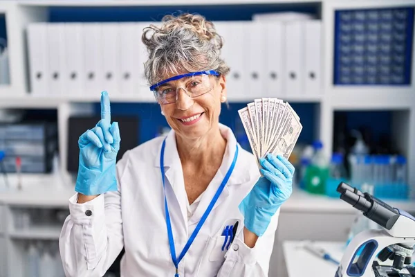 幸せな顔でアイデアや質問を指差す指で驚いてドルを保持している科学研究所で働く中世の女性 ナンバーワン — ストック写真